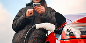 A woman is using a cell phone while charging her electric car