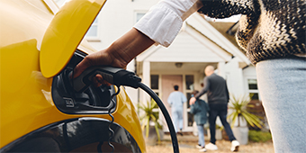 A woman is charging her electric car in front of a house