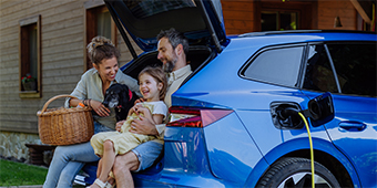 A family is sitting in the back of a blue car while it is being charged