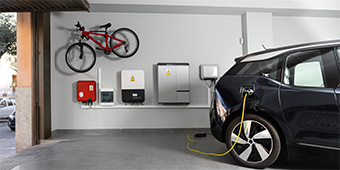 A car is being charged in a garage with a bicycle hanging on the wall