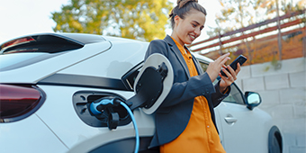 A woman is charging her electric car and looking at her phone