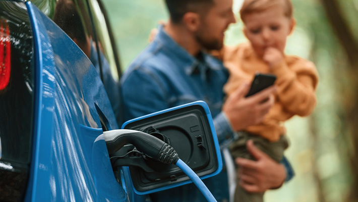 A man is holding a child while charging an electric car