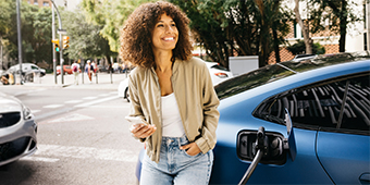 A woman is standing next to an electric car that is being charged