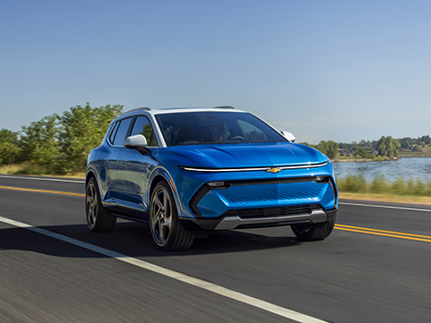 A blue car is driving down a road next to a body of water