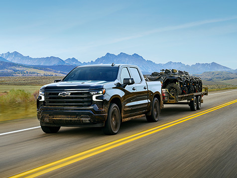 Black Chevrolet Silverado towing a trailer down a highway