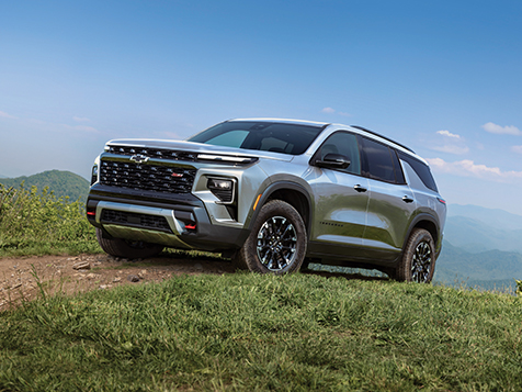 A rugged silver Chevrolet Traverse is parked on a grassy mountain slope