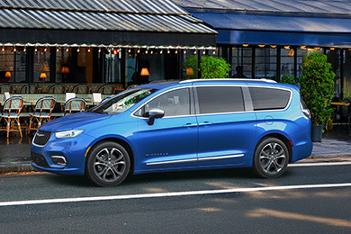 A blue Chrysler Pacifica on an urban street next to a cafe