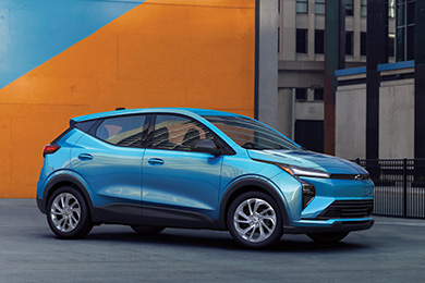 A light blue Chevrolet Bolt against a vibrant orange and blue urban wall