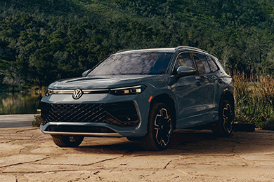 A gray Volkswagen Tiguan is parked on a dirt road in a lush, mountainous setting