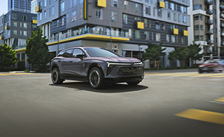 A grey Chevrolet Blazer EV is driving down a city street in front of a building