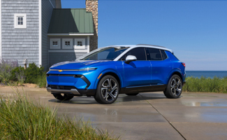 A blue Chevrolet Equinox EV is parked in front of a house next to the ocean