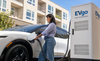 A woman is plugging an EV charger into her white Chevrolet Equinox EV at an EVgo charging station