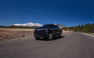 A black Chevrolet Silverado EV is driving down a road with mountains in the background