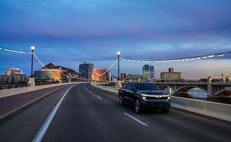 A black Chevrolet Silverado EV is driving on a bridge