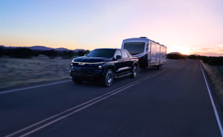 A Chevrolet Silverado EV is towing a trailer down a road at sunset