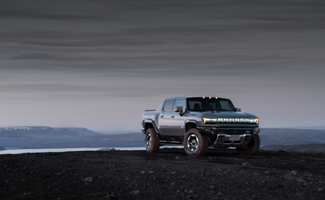 A GMC HUMMER EV SUV is parked on top of a hill with mountains in the background