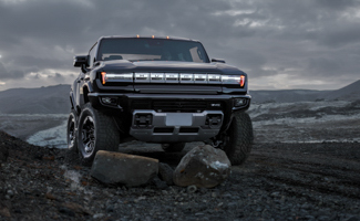 A black GMC HUMMER EV SUV is driving over a pile of boulders