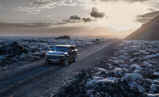 A GMC HUMMER EV SUV is driving down a dirt road surrounded by rocks