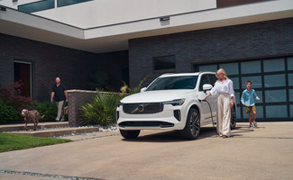 A woman charges a white Volvo XC90 parked in the driveway of a house