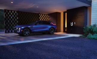 Blue Cadillac LYRIQ parked in a modern carport with an EV charger at dusk