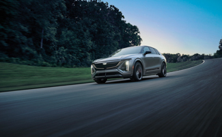 Gray Cadillac LYRIQ-V driving along a winding road at dusk