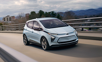 A white Chevrolet Bolt drives on an overpass with a city in the background