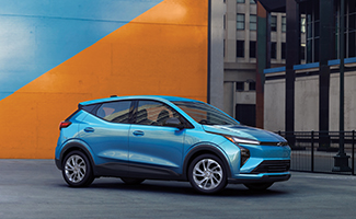 A light blue Chevrolet Bolt against a vibrant orange and blue urban wall