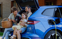 A family is sitting in the back of a blue car while it is being charged