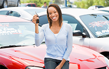 A woman is holding a car key in front of a red car