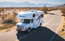 A white rv is driving down a desert road