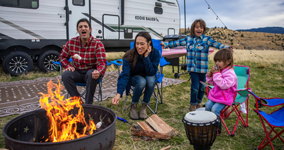A family is sitting around a fire pit in front of a RV