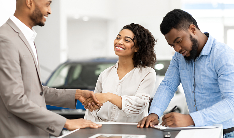 A man and woman are shaking hands with a car dealer in a car showroom