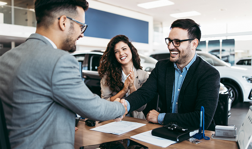 A man is shaking hands with a couple in a car showroom